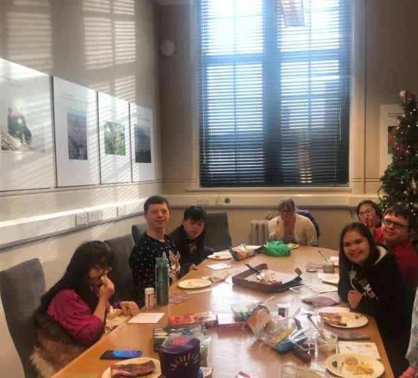 Members of the Our Voice Our Choice group enjoying their celebratory pizza lunch sitting around a large table.