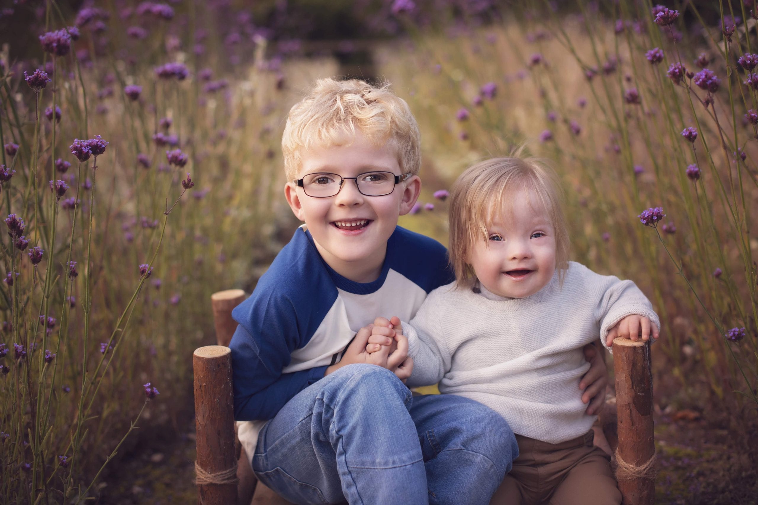 Two brothers sit in a meadow. The younger boy has Down syndrome. Photo credit www.photographybylorna.co.uk