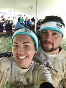 A couple pose for a selfie after completing an obstacle challenge. They are both wearing muddy DSA t-shirts