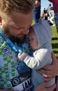 A man in a DSA running vest with a medal round his neck holds a baby, who has Down syndrome.