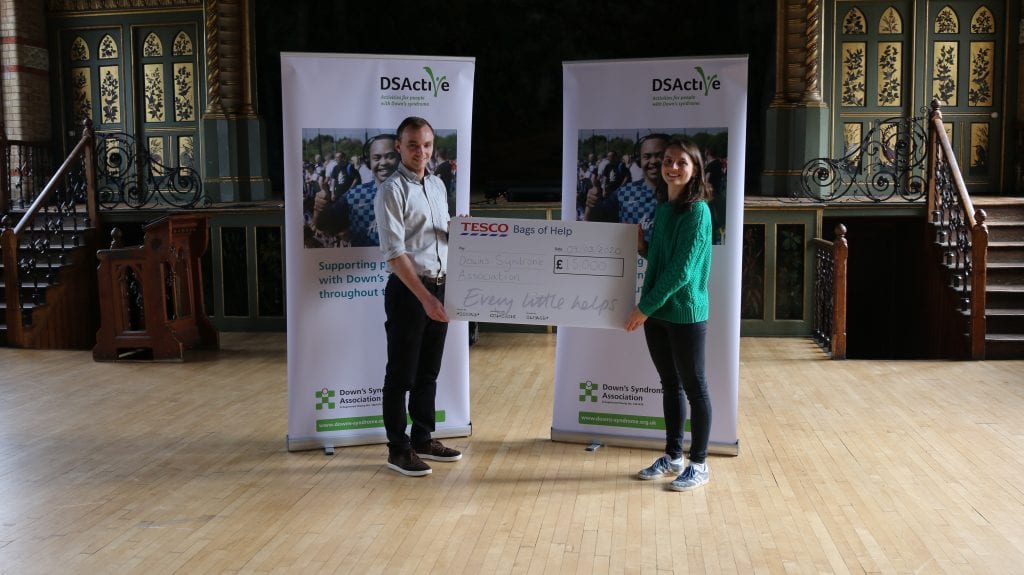 DSActive Project Manager Alex Rawle and a representative of Tesco hold an oversize cheque in front of two DSActive banners
