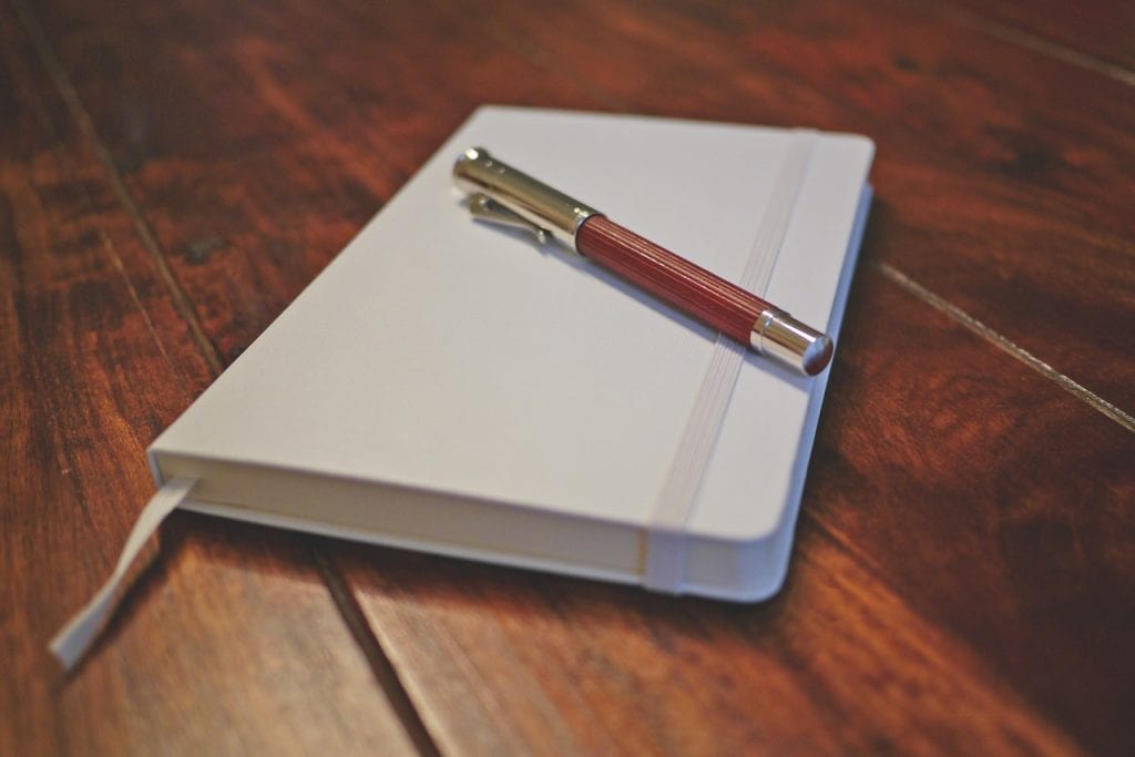 A closed note book with a pen resting on top of it