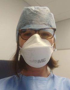 A woman with glasses in hospital PPE, gown, mask and head covering