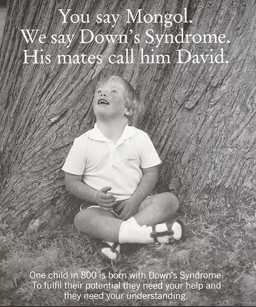 A campaigning poster of the 1980s from the DSA. The poster shows a small boy who has Down's syndrome sitting cross-legged at the bottom of a tree. The caption reads 'You say Mongol. We say Down's syndrome. His mates call him David.