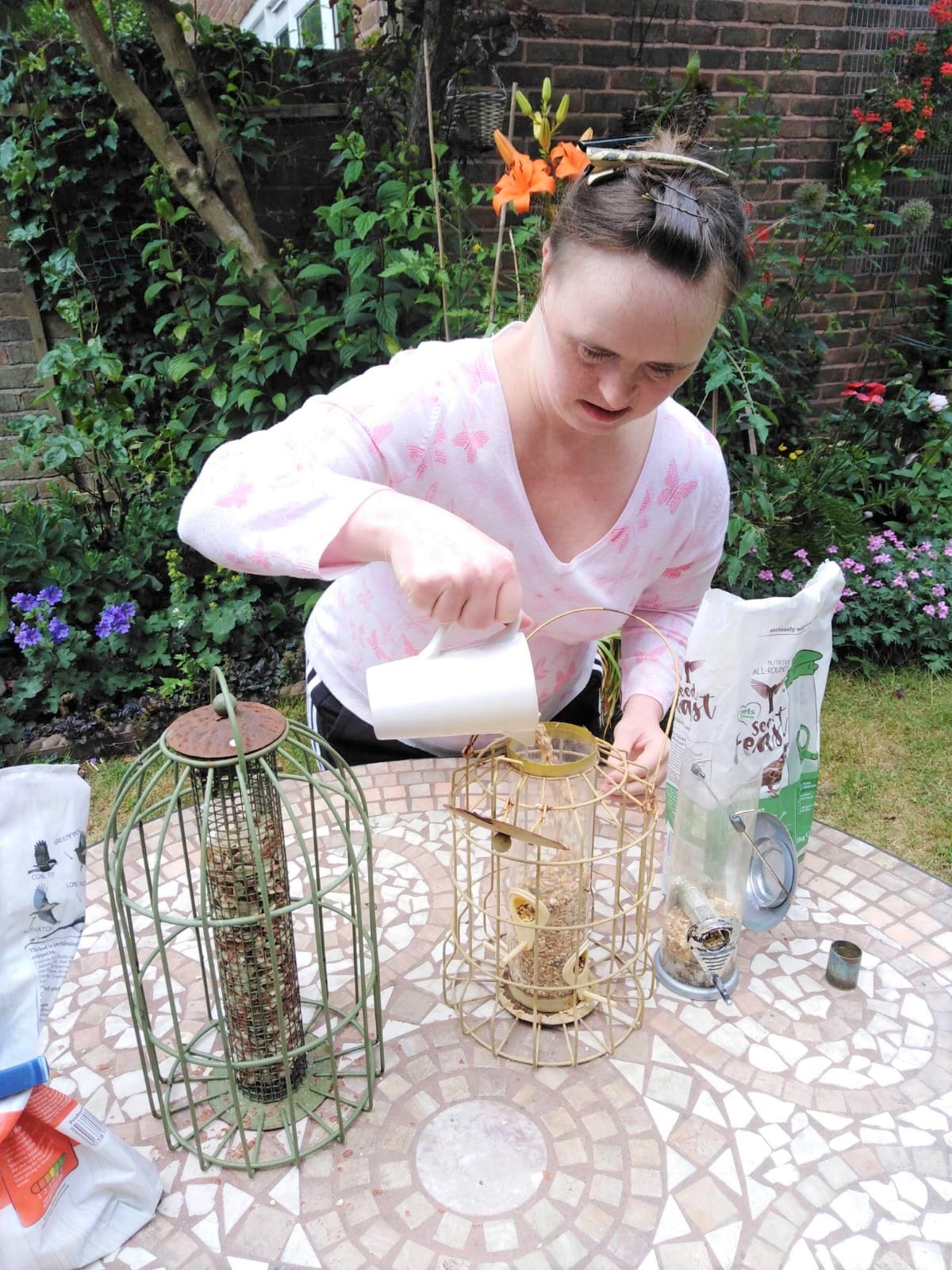 A woman fills bird feeders with seeds. She has Down's syndrome.