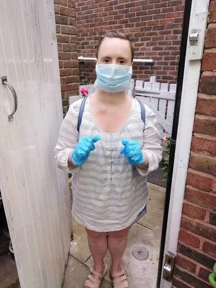 A woman stands in a doorway wearing gloves and a face mask. She has Down's syndrome