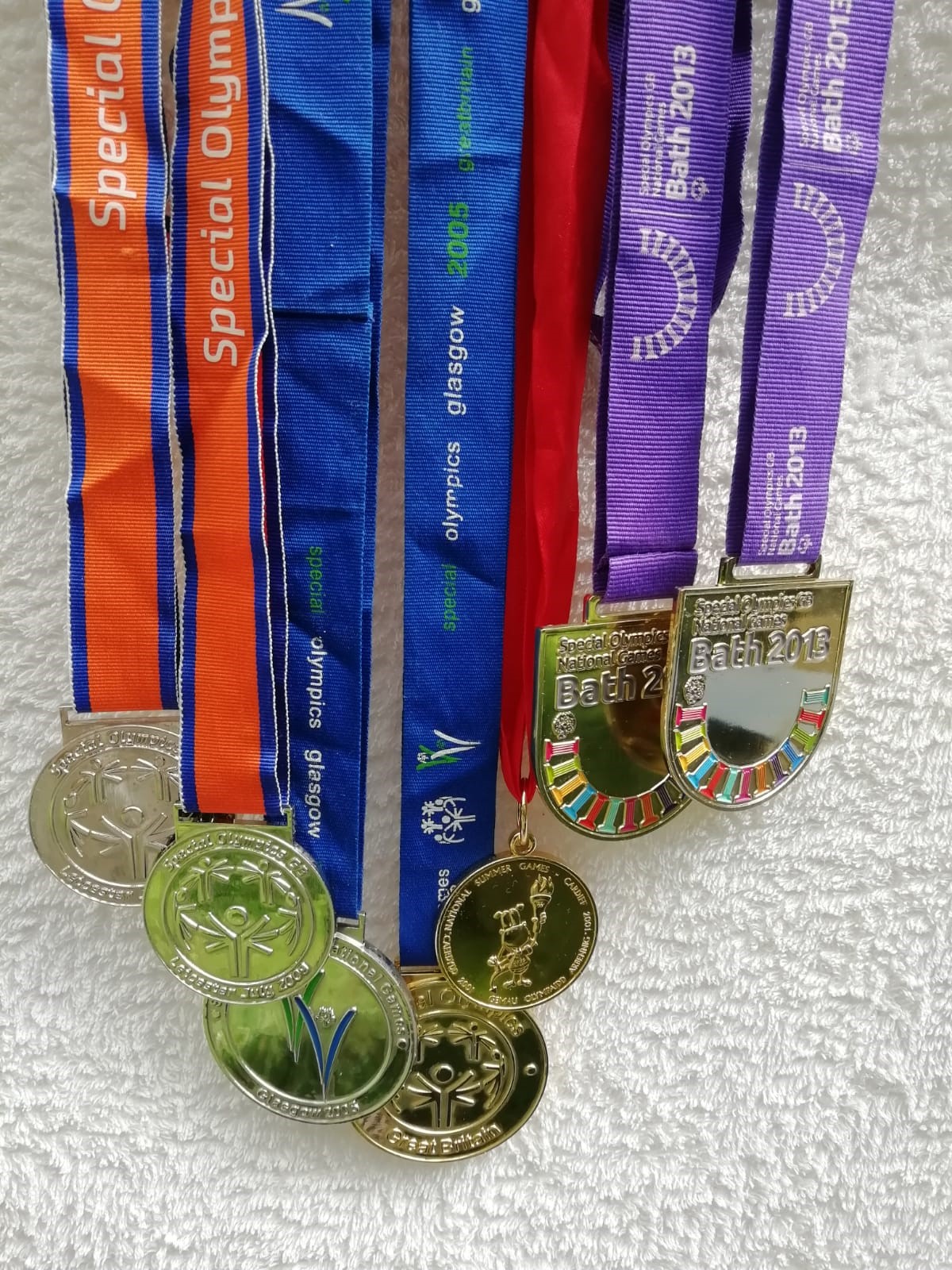 Seven sports medals hang from their ribbons against a wall