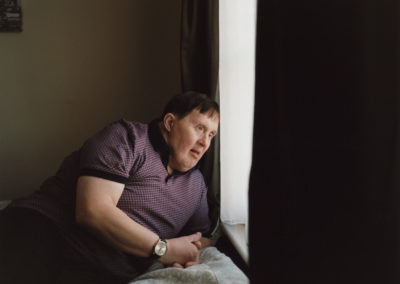 A man who has Down's syndrome reclines on a bed. He is looking out of a window.