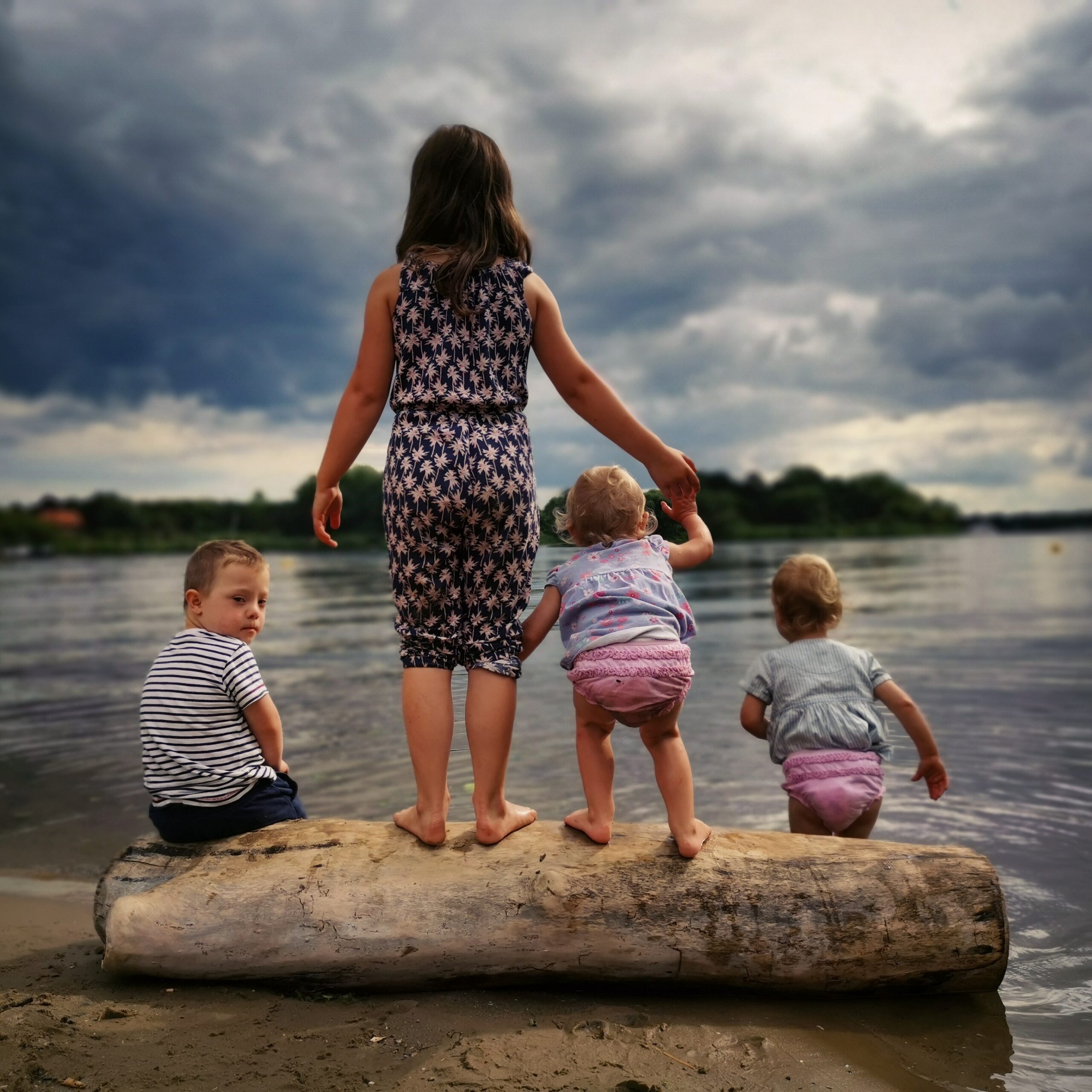 A group of four children stand on the edge of a lake.