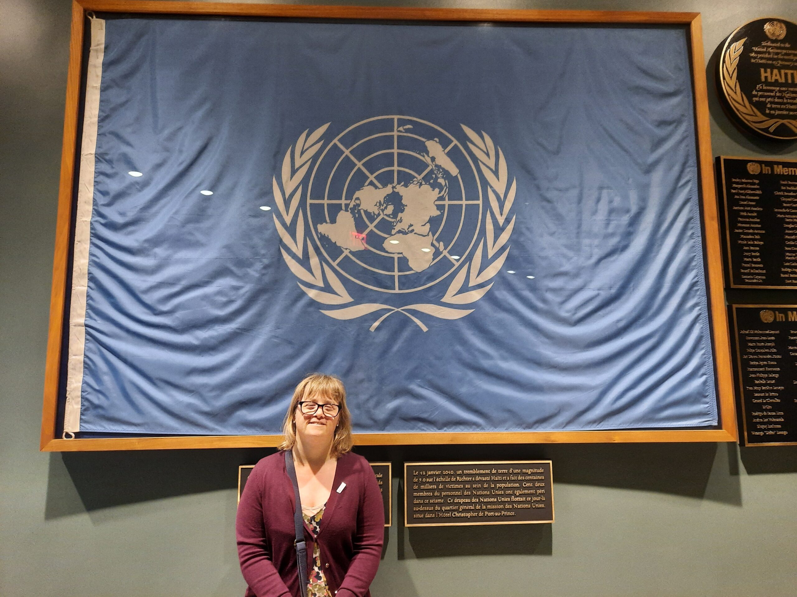Emma, a woman who has Down's syndrome, stands in front of a huge framed flag of the United Nations.