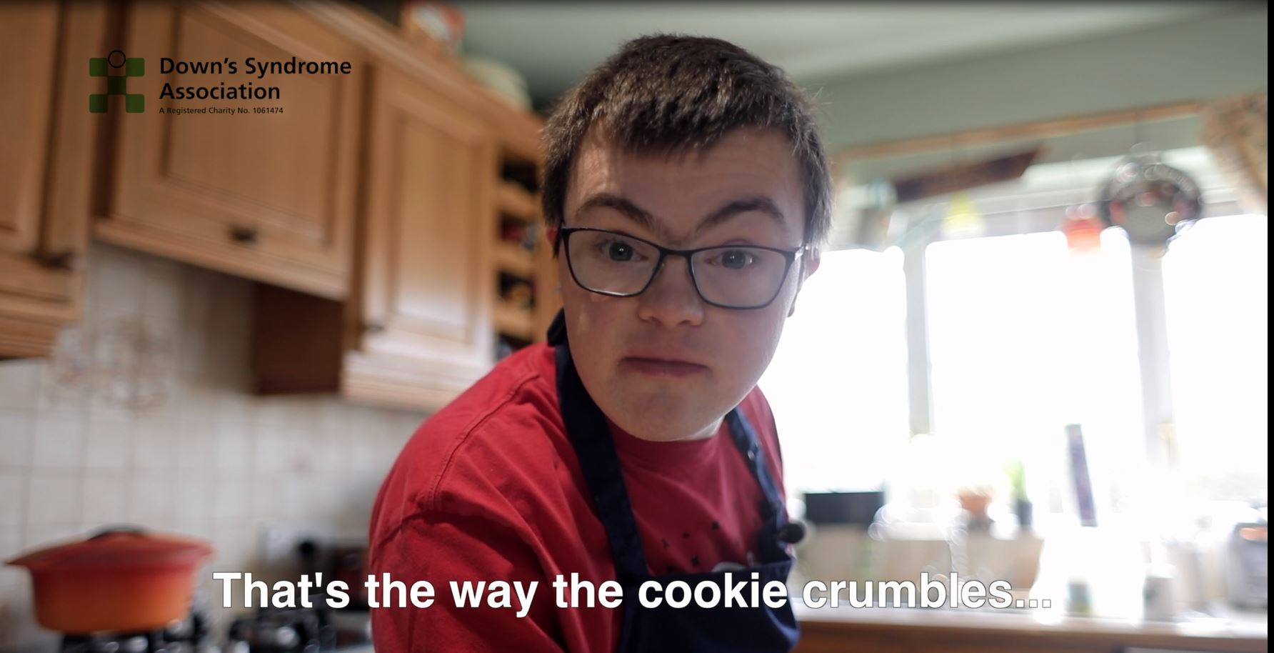 A young man looks directly at the camera. It's a screen grab from a film and the subtitles say 'That's the way the cookie cumbles.' 
