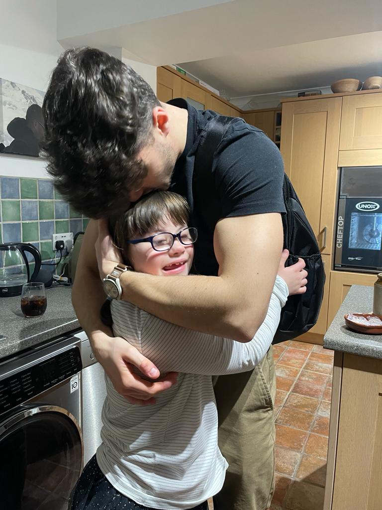 A young man hugs a girl with Down's syndrome in a kitchen.