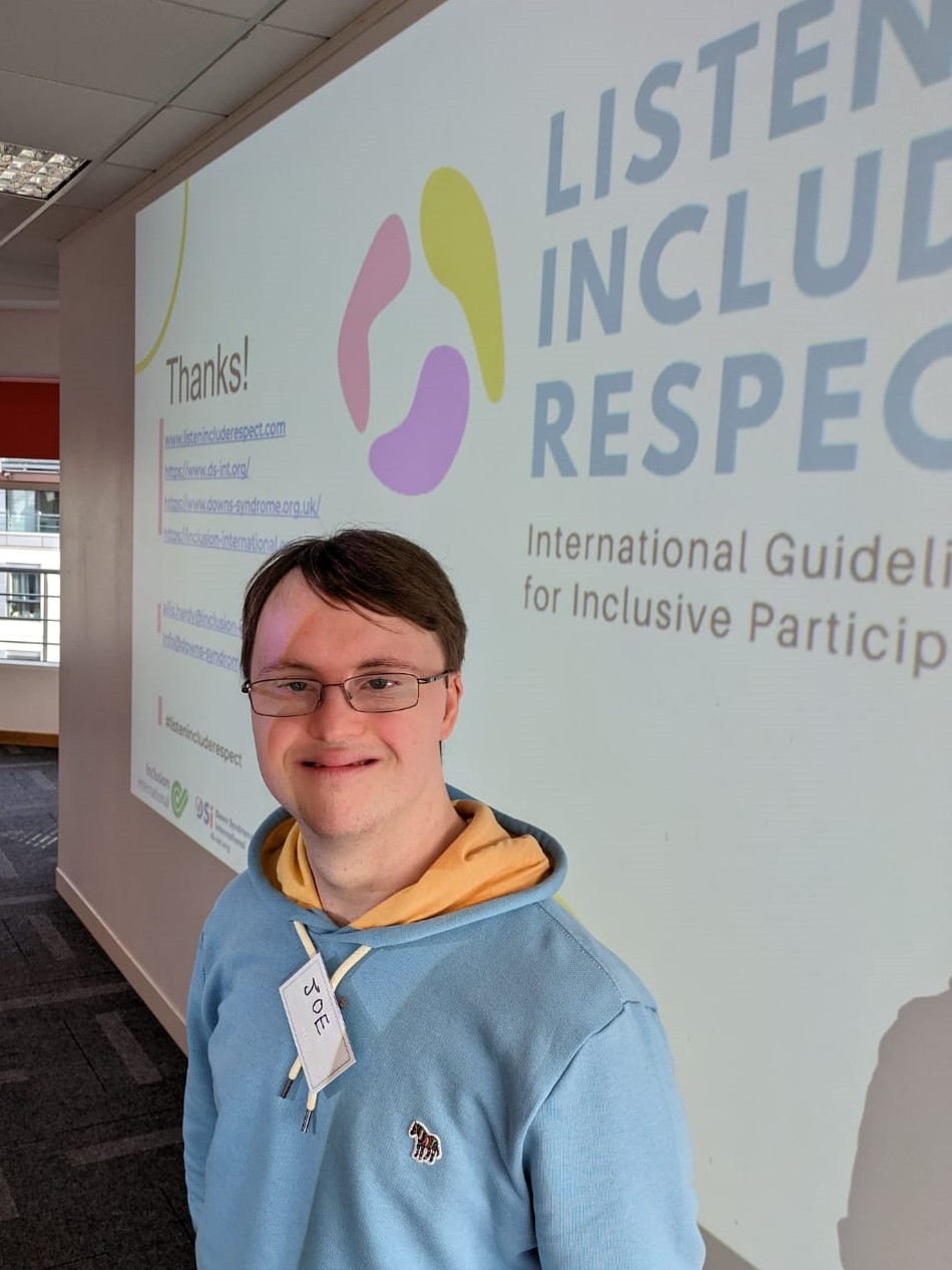 Man who has Down's syndrome smaling in front of a Learning Disability England backdrop