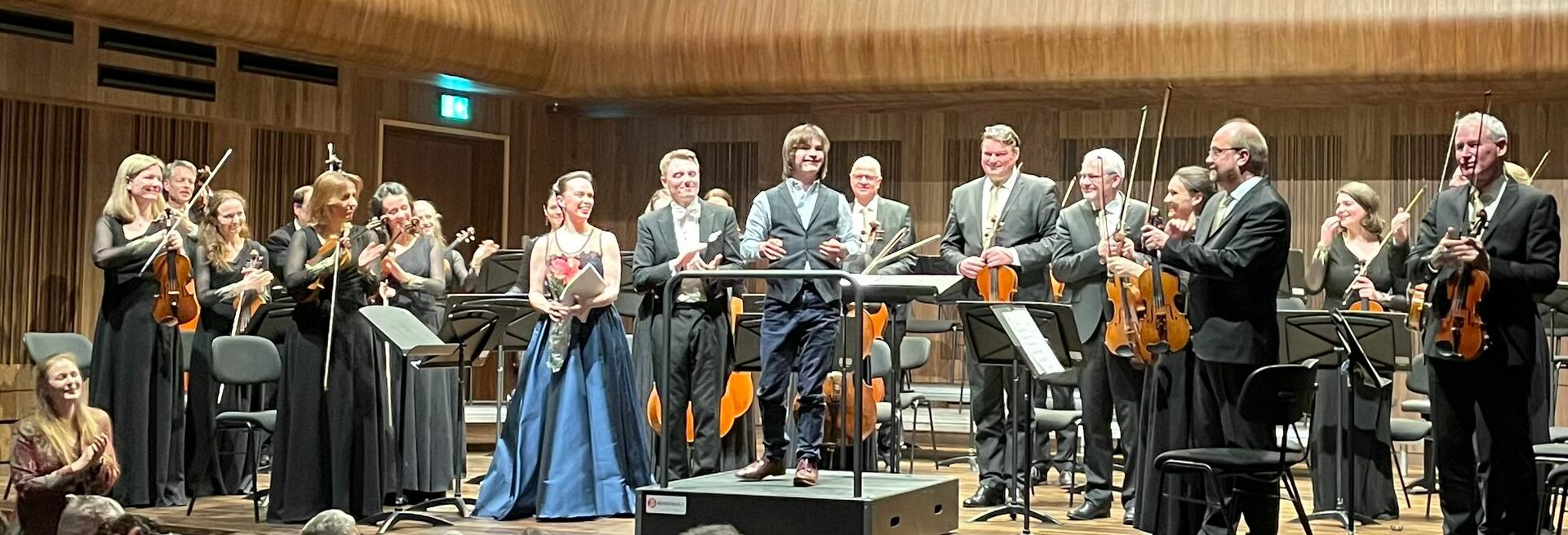 Ethan Stein on a podium surrounded by an orchestra, all standing