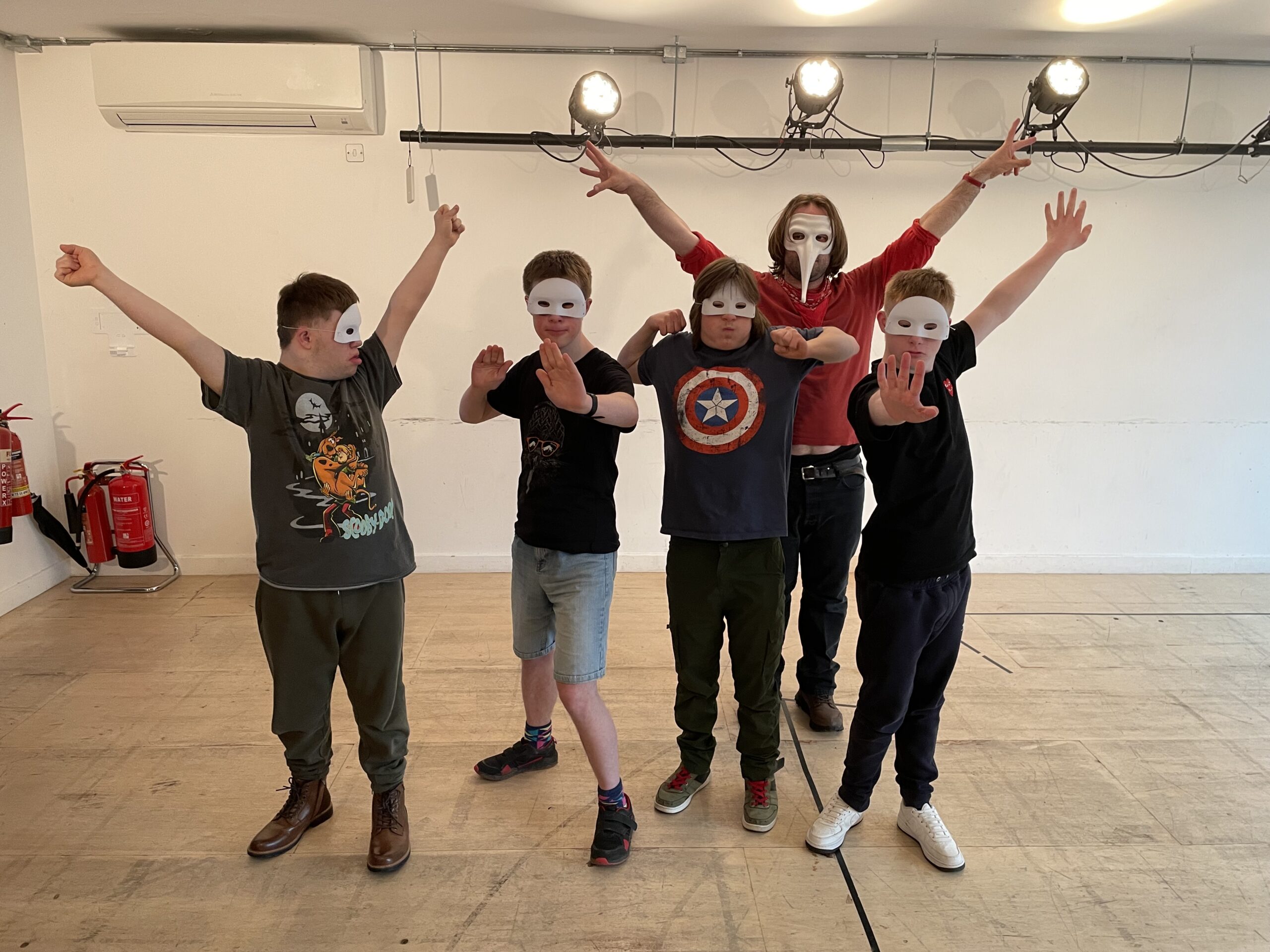 Ethan with a group of young actors, wearing masks, with their arms in the air.